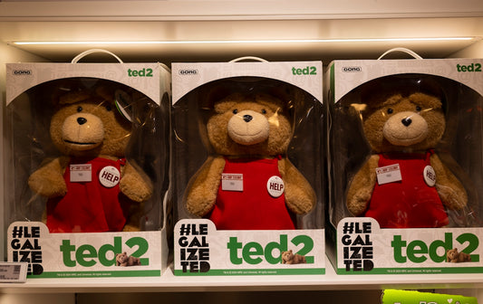 Three teddy bears in boxes wearing red overalls.